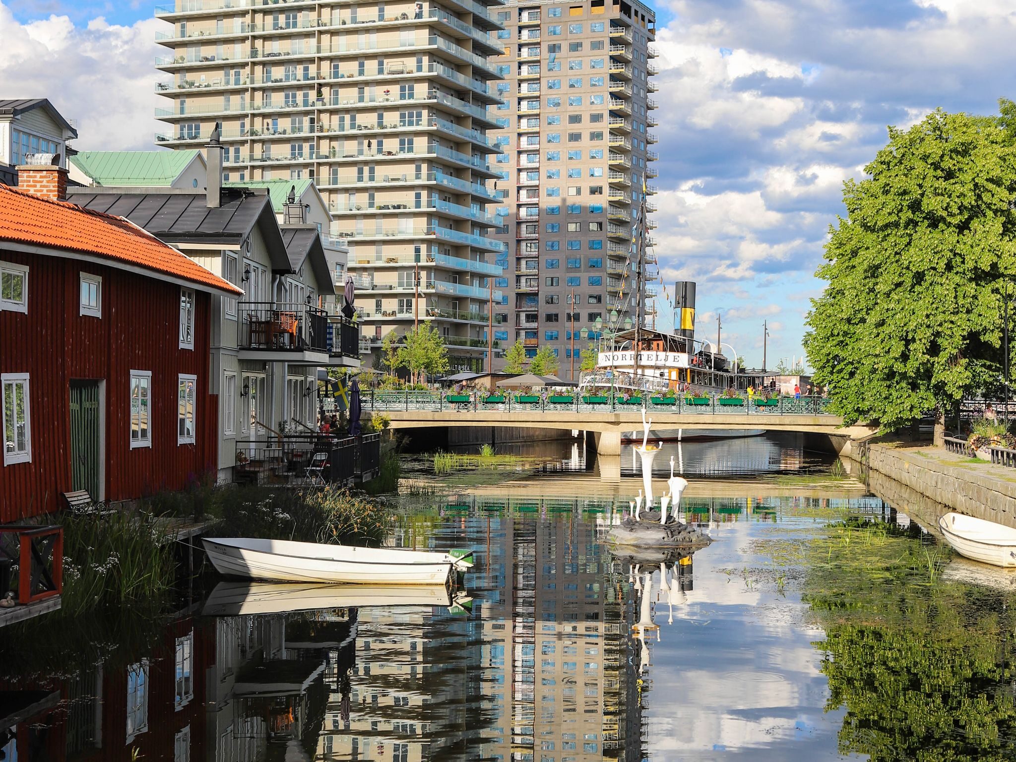 Scenic view of Norrtälje creek with modern skyscrapers reflecting on water, vibrant summer day.