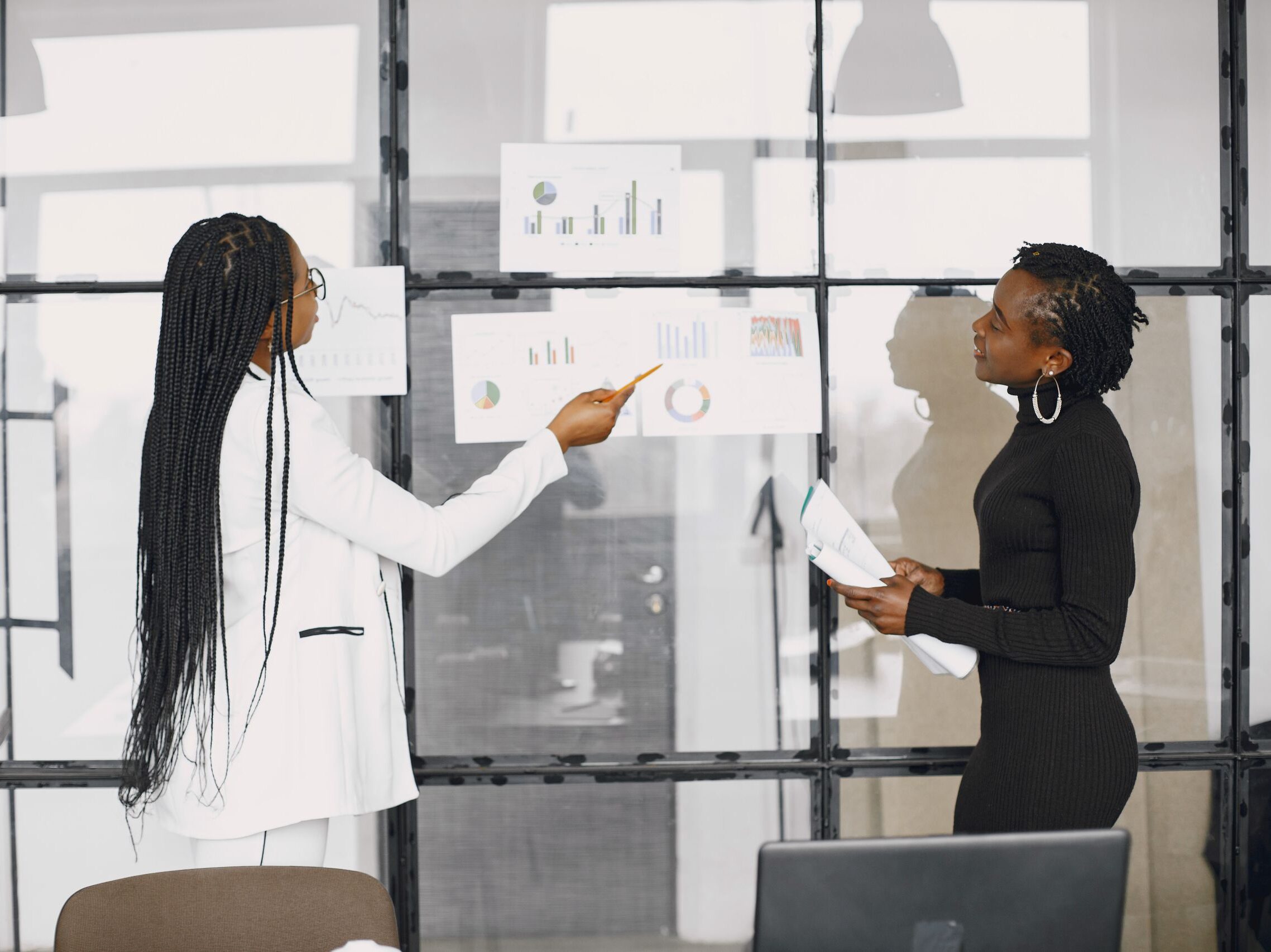 Two businesswomen discussing financial charts in a modern office setting.