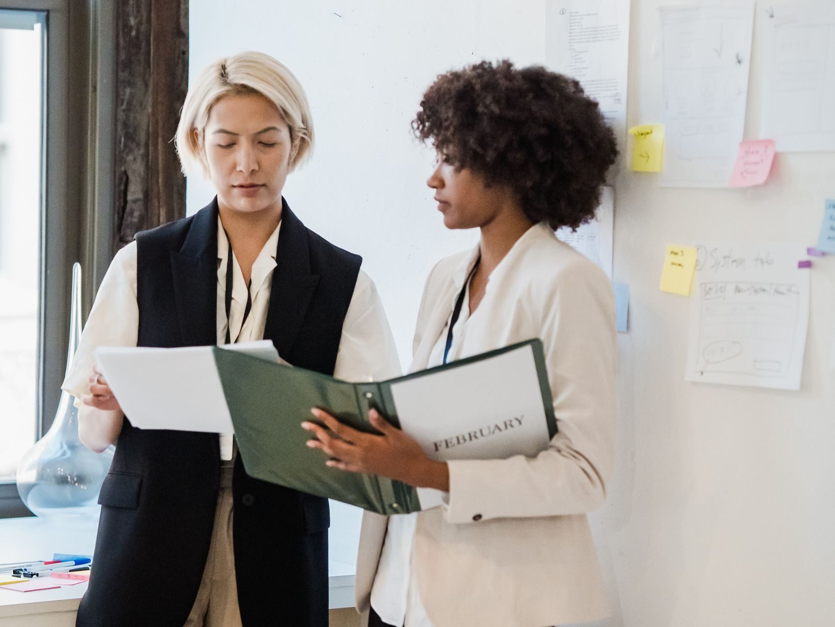 Two professional women reviewing documents in a modern office setting.